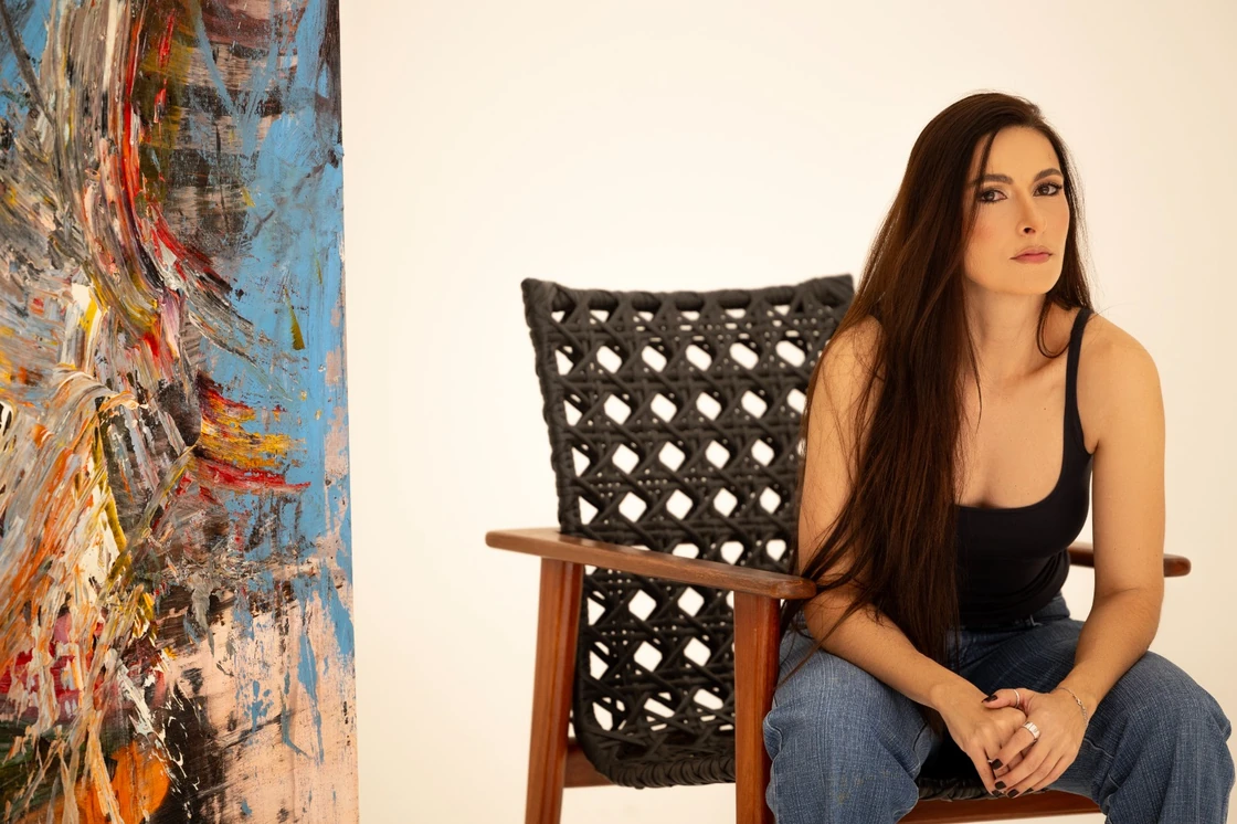 Chyara Feer sentada ao lado de uma de suas pinturas.